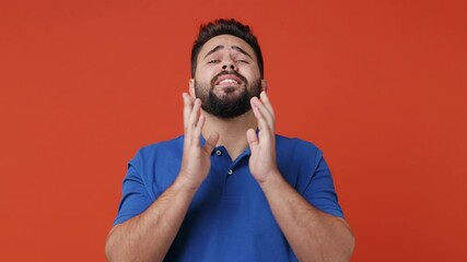 Poster - Young bearded brunet man 20s years old wears blue t-shirt hold hands folded in prayer begging about something making wish keep fingers crossed isolated on plain red orange background studio portrait