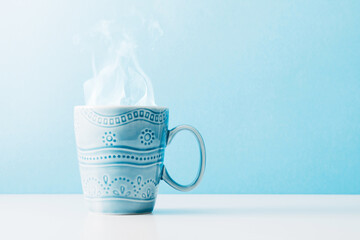 Steaming cup with tea on pastel blue background. Blue mug with cappuccino and steam. Front view, copy space