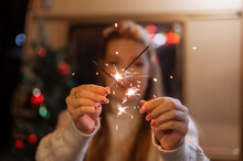 Sparklers Bengal Fire Stick In Female Hands Holding Woman In Knitted Wool White Cozy Sweater On The Background Of A Camping Trailer House Outdoor On New Year And Christmas Eve Night. Sparkling Sparks