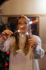 sparklers bengal fire stick in female hands holding woman in knitted wool white cozy sweater on the background of a camping trailer house outdoor on new year and christmas eve night. sparkling sparks