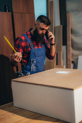 Wall Mural - Young male carpenter working in workshop and using smartphone