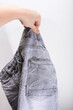 Hand holding used old grey frayed jeans against white background, throwing out old clothes and repalcing it to new