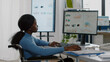 © DC Studio - African disabled invalid manager woman working at pc showing data prosessing on desktop for project regarding economy looking at financial documents checking graphs, reading raports in business office