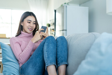 Wall Mural - Asian beautiful woman sit on sofa and chat on mobile phone in house.