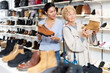 © JackF - Female sales consultant helps a mature european woman choose winter shoes in a store