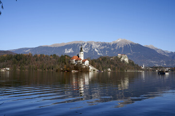 Sticker - Scenic shot of a church surrounded by a lake, a forest, and mountains in Slovenia