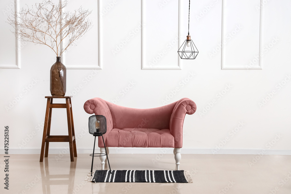 Pink armchair, lamp and vase with branches near light wall