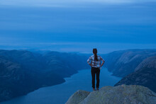 Young Woman Hiker Standing On A Rocky Hill And Looking Over Lysefjorden In The Evening In Norway
