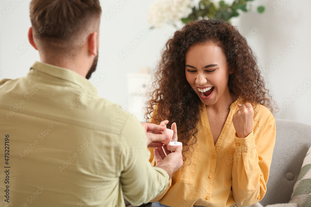 Young man proposing to his happy girlfriend at home