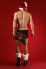 Poster - Sexy young man in Santa hat, underwear and with Christmas gift on color background, back view