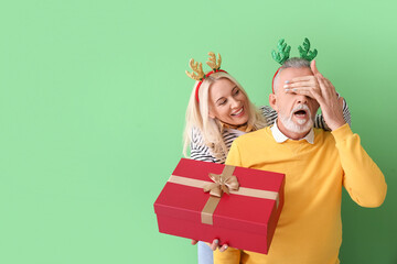 Sticker - Happy mature woman greeting her husband on Christmas eve against color background