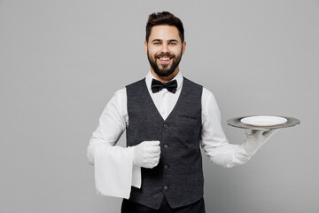 Wall Mural - Young happy fun barista male waiter butler man 20s wear white shirt vest elegant uniform work at cafe hold empty dish meal plate isolated on plain grey background studio. Restaurant employee concept.