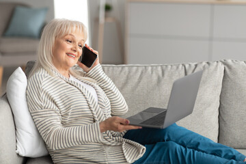 Wall Mural - Smiling mature woman working and talking on phone at home