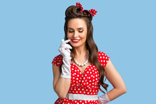 Sensual Young Pinup Woman In Retro Red Polka Dot Dress Touching Her Face And Smiling Mysteriously On Blue Background