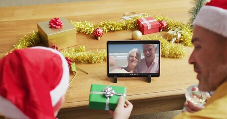 Poster - Caucasian father and son with santa hats using tablet for christmas video call with couple on screen