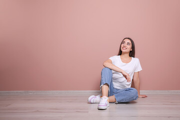 Wall Mural - Young woman sitting on floor near pink wall indoors. Space for text