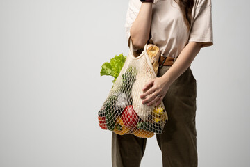 Wall Mural - Female hand with mesh eco bag with groceries on grey background. Zero waste concept.