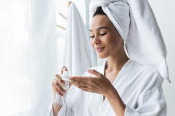 Wall Mural - smiling african american woman in towel holding bottle with cleanser and cotton pad in bathroom