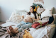 © Ilona - Cute young pregnant woman relaxes lying on the bed and listening to music on wireless headphones.