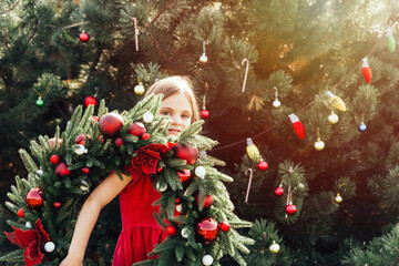 Wall Mural - Merry Christmas. Portrait of happy funny child girls in Santa hat with Christmas wreath. Happy Holidays. Fairy Magic. Happy kid enjoying holiday. Christmas in July