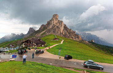 Wall Mural - Summer scenery of majestic mountains on a moody cloudy day with rocky peaks in background & a highway through the green grassy hillside at Giau Pass, Cortina d'Ampezzo, Dolomites, South Tyrol, Italy