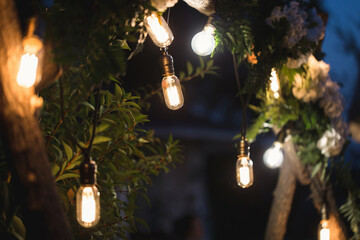 Wall Mural - Burning light bulb hanging from a tree in a garden decoration wedding celebration