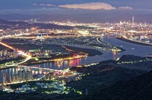 Aerial Panorama Of Taipei City In A Blue Gloomy Night, With View Of Guandu Plain, Bridges Over Tamsui River, Taipei 101 Tower Among Buildings & City Lights In XinYi District Downtown At Dusk