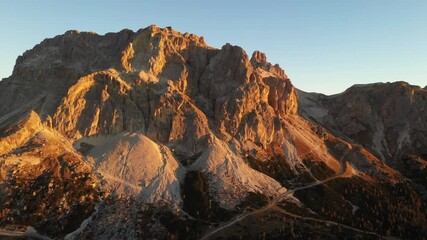 Wall Mural - Aerial flight over the autumn Dolomite mountains at sunrise time. Rocks covered by orange larches glowing by sunset light. Falzarego pass, Trentino Alto Adige, , Dolomites Alps, Italy. UHD 4k video