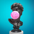 Funny concept illustration from 3d rendering of classical black marble head sculpture blowing a pink chewing gum bubble. Isolated on blue background.