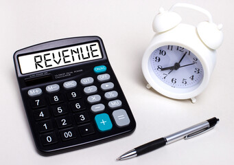 Fototapete - On the light table there is a black calculator with the text REVENUE on the scoreboard, a pen and a white alarm clock. Business concept
