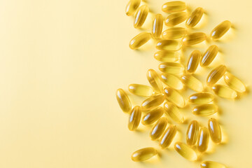 Transparent capsules with the women health food supplement of evening primrose oil. Vegan soft gels are sprinkled on a yellow background. Top view, copy space.