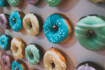 Sticker - Closeup shot of colorful donuts hanging from a pink wall in a cafe