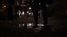 The A Man Walks Through A Puddle Along A Dark Trail Path On A Rainy Night.