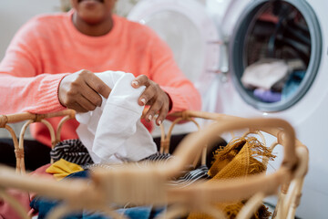 Wall Mural - Putting a white t-shirt in the wash, a woman's hands remove clothes from a wicker basket, a girl sits on the floor doing household chores, throws things into the washing machine