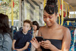 © ABCreative - Dark-skinned beautiful woman with dreadlocks tied up in bun sits on public transportation bus smiling looking at phone texting friends browsing social media going out on town with boyfriend