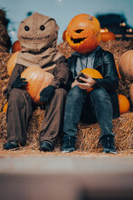 A Guy With A Pumpkin Head Sits Next To A Scarecrow