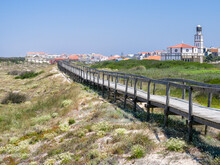 Portugal, Costa Nova. Beach And Board Walk At Costa Nova Beach Resort With The Clock And Bell Tower Of Our Lady Of Health Church In The Distance Near Aveiro.