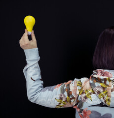 Canvas Print - Woman holding a yellow idea lamp as a symbol of having an idea against a black background