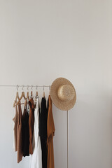 Wall Mural - Aesthetic minimalist fashion influencer blog concept. Female dress, tops, t-shirts, straw hat on clothing rack on white wall. Fashion women clothes