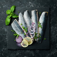 Salted herring with onions and spices on a black stone plate. Top view. On a stone background.