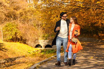 Sticker - Beautiful young couple holding paper cups with drink and walking in autumn park