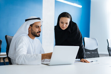 Wall Mural - Man and woman with traditional clothes working in a business office of Dubai. Portraits of successful entrepreneurs businessman and businesswoman in formal emirates outfits. Concept about middle east