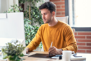 Fototapete - Graphic designer using a pen tablet while working with computer in modern startup office.