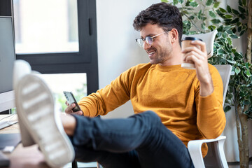 Fototapete - Graphic designer working with computer while using smartphone and drinking coffee in modern startup office.