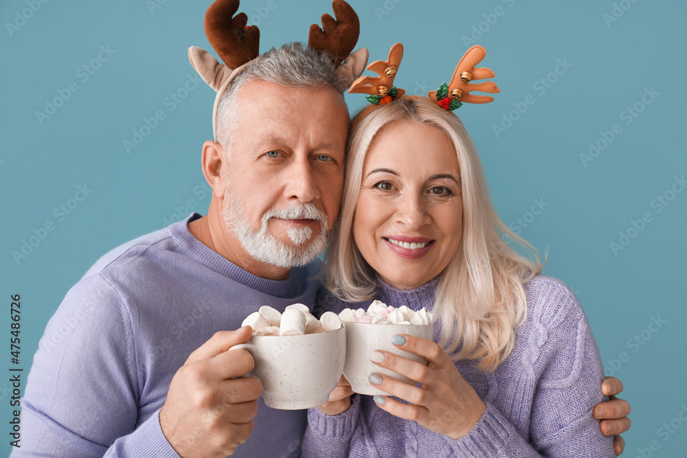 Happy mature couple with hot chocolate on color background