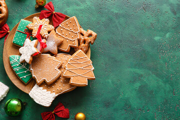 plate with tasty gingerbread cookies and christmas decorations on green background