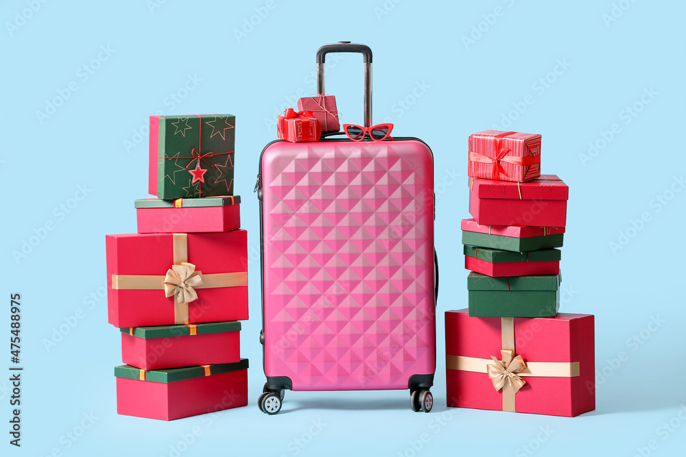 Pink suitcase with sunglasses and Christmas gift boxes on blue background
