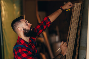 Wall Mural - Young male carpenter working in workshop and measuring with meter