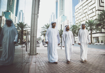 Wall Mural - Image of a group of friends from the emirates meeting in Dubai.  Young adults wearing the traditional local white dress spending time in the city center. Concept about middle eastern cultures 