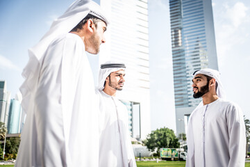 Wall Mural - Image of a group of friends from the emirates meeting in Dubai.  Young adults wearing the traditional local white dress spending time in the city center. Concept about middle eastern cultures 